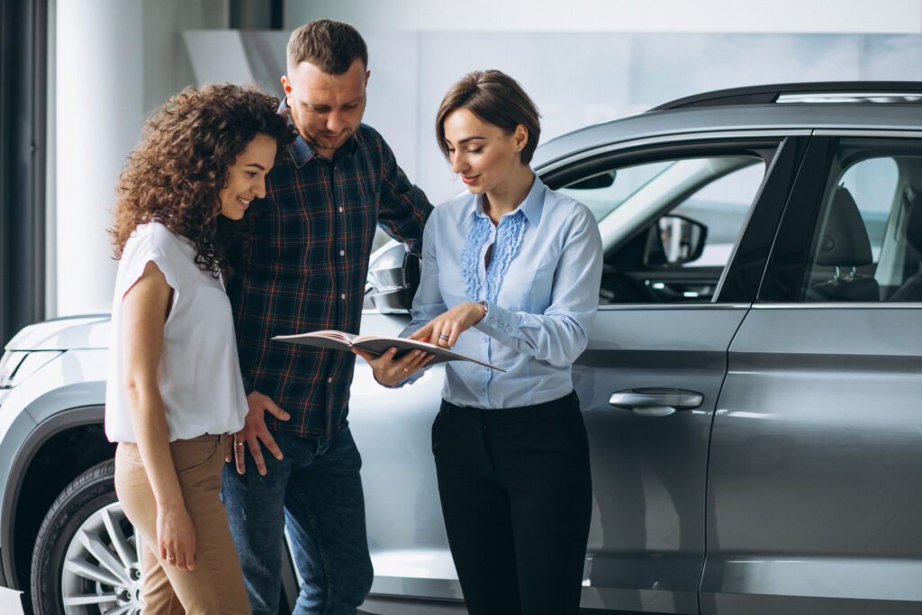 Young couple talking to a sales person in a car showroom - MOTOFLIP Free photo young couple talking to a person selling a car