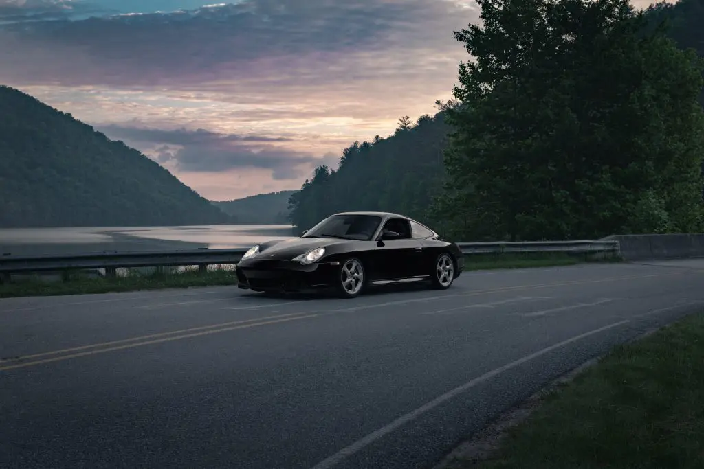 A black Porsche coupe on a bridge passing a river during evening time